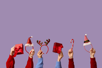 Female hands holding Christmas headbands with gift boxes and candy cane on lilac background