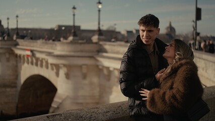 A romantic couple is embracing on a bridge in Paris France The urban scene features beautiful architecture and can be used for travel photography Valentine's Day promotions and tourism campaigns.