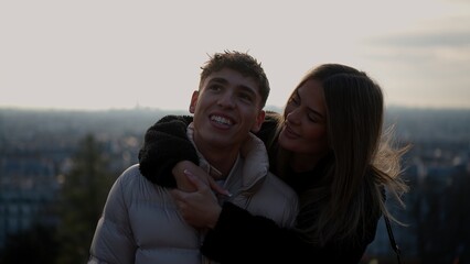 A romantic young couple embraces with the Paris cityscape in the background during sunset. This image conveys love and affection in France ideal for travel and relationship concepts.