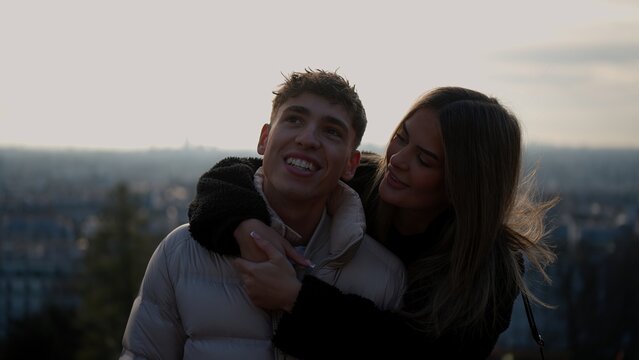 A romantic young couple embraces with the Paris cityscape in the background during sunset. This image conveys love and affection in France ideal for travel and relationship concepts.