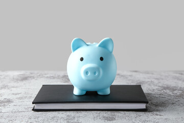 Piggy bank with book on grunge grey table near wall