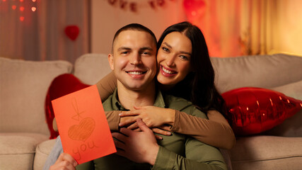Happy Valentine's Day. Excited lady embracing man, giving greeting card to her beloved husband,...