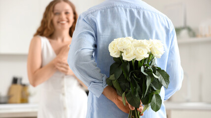 Young man with white roses for his girlfriend in kitchen, back view
