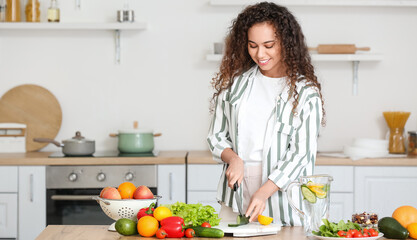 Young African-American woman cutting vegetables in kitchen