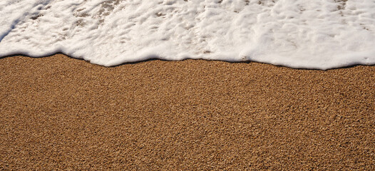 Top down view of the shoreline where the foamy white wave meets the brown sand creating a natural border and texture contrast