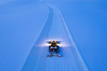 Overhead view of a snow groomer creating tracks on a vast snow covered landscape at dusk