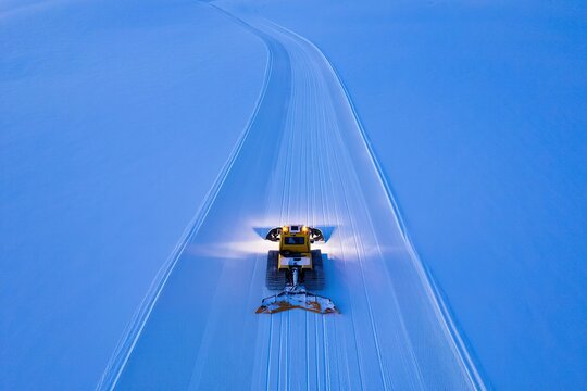 Overhead view of a snow groomer creating tracks on a vast snow covered landscape at dusk - Powered by Adobe