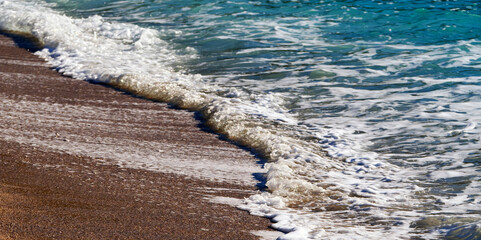 A dynamic horizontal view of a curling white wave breaking as it rolls onto the textured brown and...