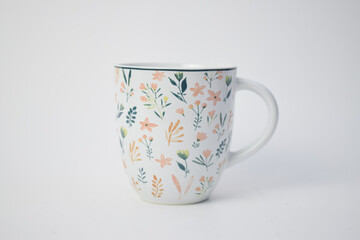 White ceramic coffee mug decorated with colorful hand-painted flower and leaf patterns, isolated on white.