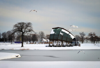 Tranquil winter landscape at a wildlife sanctuary pond with seagulls flying over the Dome at Seaside Park at sunset in snow in Bridgeport, Connecticut, United States