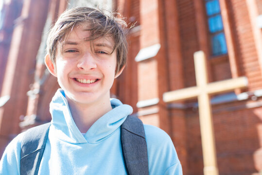 Portrait of a smiling 13 year old boy with a backpack in front of a Catholic church.	