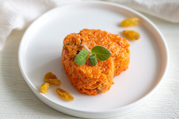 Carrot casserole with dried fruits in heart shape on white plate