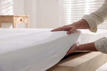 Man touching soft mattress on bed indoors, closeup