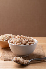 Cooked Thai brown rice in a bowl with spoon on wooden background, Healthy eating