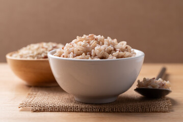 Cooked Thai brown rice in a bowl with spoon on wooden background, Healthy eating
