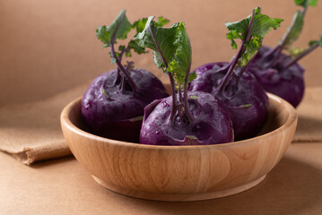 Purple kohlrabi or turnip cabbage in wooden bowl on brown background