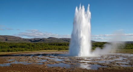 A geyser erupts with a massive column of water against a scenic backdrop