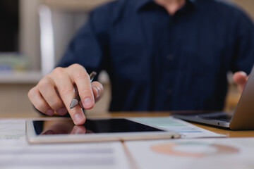 businessman working with tablet and laptop, holding pen and analyzing digital data and financial charts in modern office environment. Digital transformation in business concept.