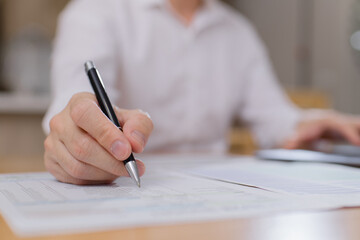 Close-up of businessman holding smartphone and writing on paper document, multitasking during data review or financial analysis in office workspace Modern business communication concept.