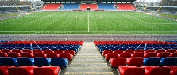 A view of an empty stadium with red and blue seating and a green field