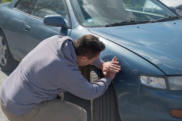 A Caucasian man tries to repair damage to a car body with his hands.