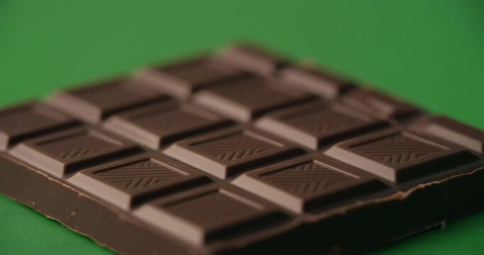 A chocolate bar with a smooth surface and distinct segments on a vibrant green background