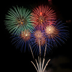 Obraz premium Vibrant fireworks exploding in the night sky with colorful bursts of green, red, blue, and orange against a dark background.