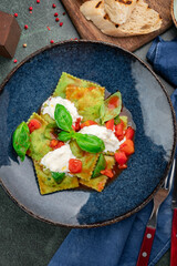Fresh green ravioli with creamy burrata, tomato sauce and basil in blue bowl. Authentic Italian pasta dish, gourmet cuisine, restaurant style.