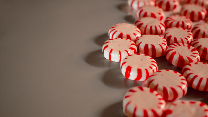 Round peppermint candies with red and white stripes are scattered on a smooth surface their glossy texture and bright color create a festive and sweet visual arrangement