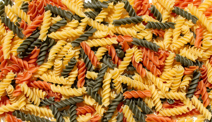Colorful spiral pasta is scattered closely together in a vibrant mix of yellow green and orange shades showing a textured and appetizing arrangement of dry pasta shapes