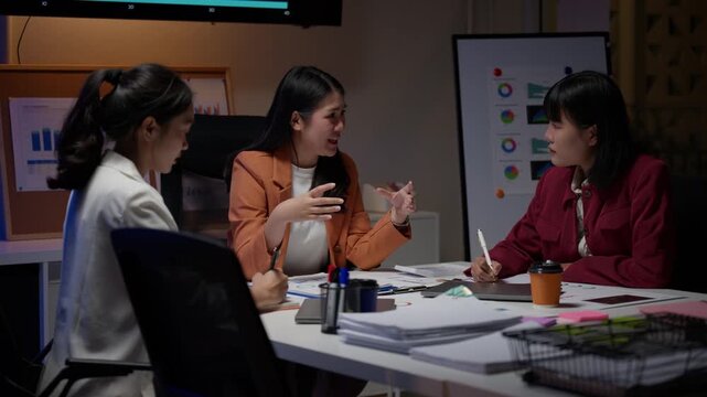 Three young asian businesswomen discussing a project during a late meeting. Professional female colleagues collaborating and working overtime