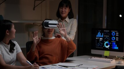 Three asian businesswomen working late, using a VR headset for a business presentation. A colleague explores data visualization in the metaverse - Powered by Adobe