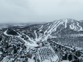 Fototapeta premium Aerial winter view of Bromont ski resort with snowy slopes, village and parking area in Quebec, Canada. g.