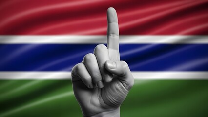 A grayscale hand with an index finger pointing up against the vibrant flag of The Gambia, symbolizing unity or victory.