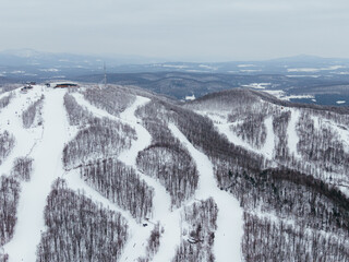 Aerial winter view of Bromont ski resort with snowy slopes, village and parking area in Quebec,...