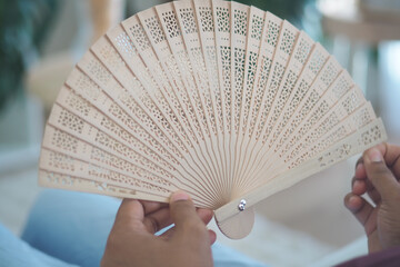 Hands holding a wooden folding fan in a simple setting