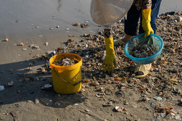 Individual collecting waste from beach shoreline with yellow gloves and buckets for environmental cleanup