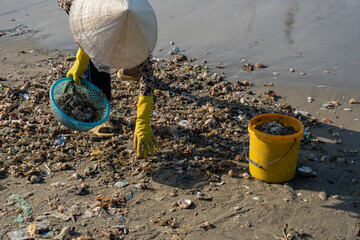 Asian woman collecting trash on beach with yellow gloves and straw hat, promoting environmental awareness