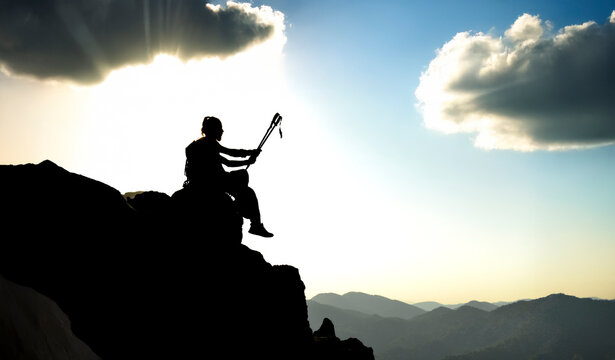 A mountaineer sitting on the cliff edge with his trekking poles at the summit, watching the view. - Powered by Adobe