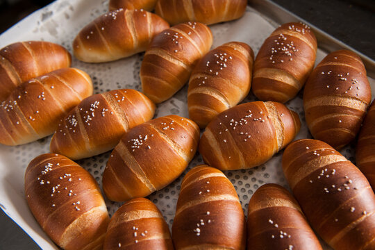 The process of baking bread: Baker using a spatula and glove to arrange freshly baked golden salt bread (Shio Pan) on a tray