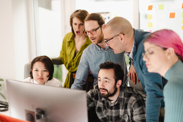 Team of businesspeople collaborating in a modern office, actively engaged in a discussion while reviewing a computer screen during a brainstorming session