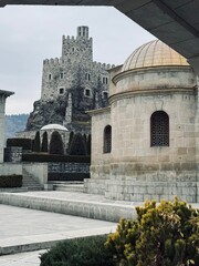 View of Lomsia Castle from Rabati Castle grounds in Akhaltsikhe, Georgia, showing the distant fortress perched on a hill amid lush greenery and historic landscape