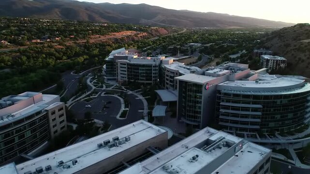 Aerial view of a large medical complex with modern buildings and parking lots surrounded by trees and mountains