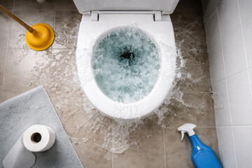 Conceptual home maintenance photo of clogged toilet emergency. Water spilling from overflowing bowl onto floor creates messy, dramatic composition from top down perspective