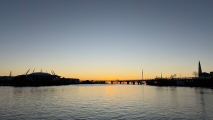 Fototapeta premium A serene sunset over a river, with silhouettes of buildings and a bridge in the foreground