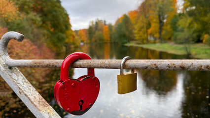 Heart-shaped red padlock on a bridge with autumn trees and river.
