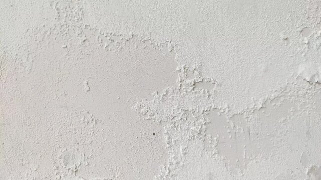 Close-up timelapse of white paint peeling and cracking on a weathered industrial concrete wall background.