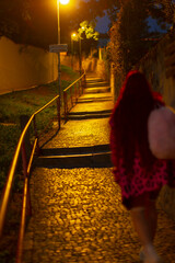 A person walking up a cobblestone path illuminated by warm street lights at night. The serene atmosphere and soft glow create a peaceful environment.