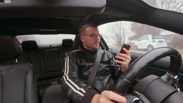 Man driving a car while staring at his smartphone, showing risky distracted driving behavior. Concept for accident danger, road safety awareness, insurance liability, and mobile phone distraction.