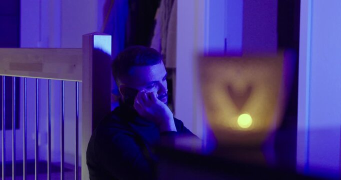 Emotional man tries to call someone he loves at night but can&rsquo;t reach them, showing frustration and heartbreak in blue-lit indoor scene. Concept for missed calls, breakup, distance